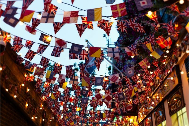 Charming alley in London adorned with colorful flags and festive lighting during sunset.